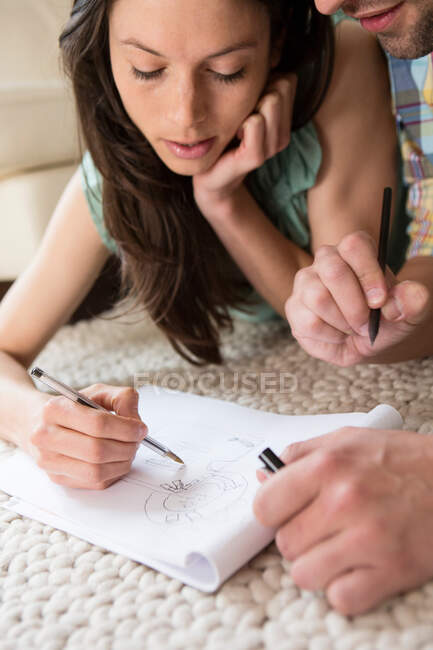Mid adult couple lying on floor sketching house plans — Stock Photo
