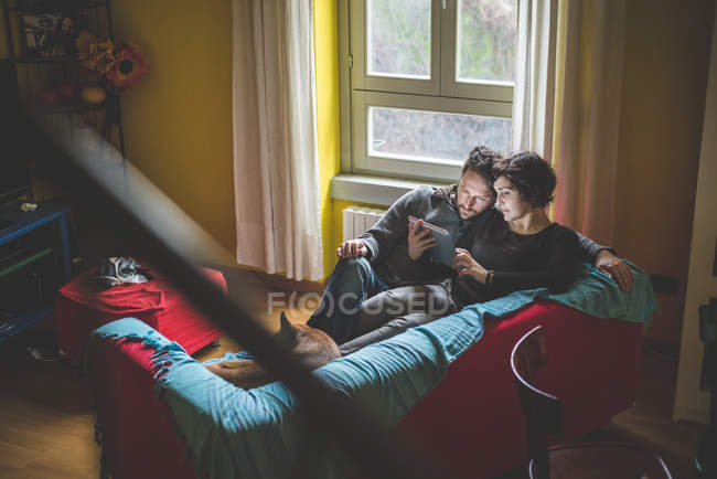 Casal sentado no sofá, olhando para tablet digital — Fotografia de Stock