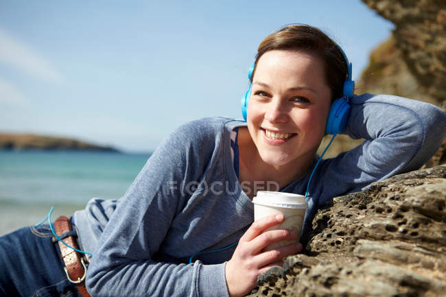 Portrait de jeune femme à la côte avec café et écouteurs — Photo de stock