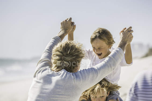 Father play fighting with sons on beach — Stock Photo