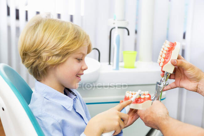 Niño en silla de dentistas aprendiendo a cepillarse los dientes - foto de stock