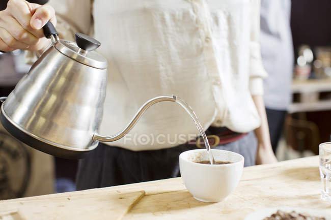Abgeschnittenes Bild einer Frau, die heißes Wasser in eine Tasse Kaffee gießt — Stockfoto