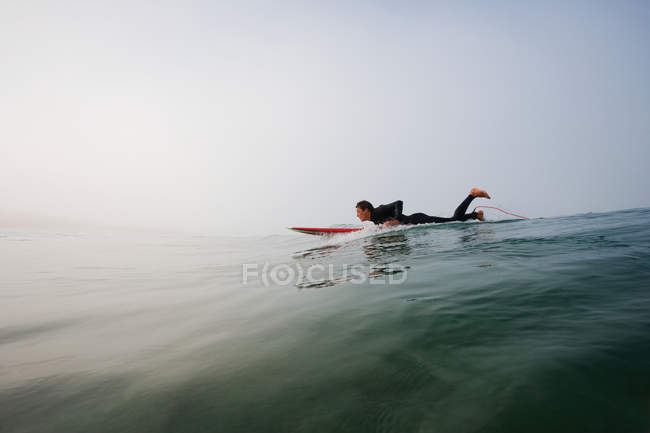 Homem deitado na prancha de surf na água do oceano — Fotografia de Stock
