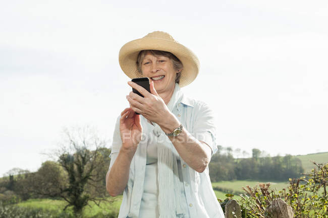 Donna anziana sorridente al messaggio sul telefono cellulare — Foto stock