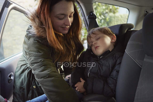 Мать убирает спящего малыша сына с заднего сидения машины — стоковое фото