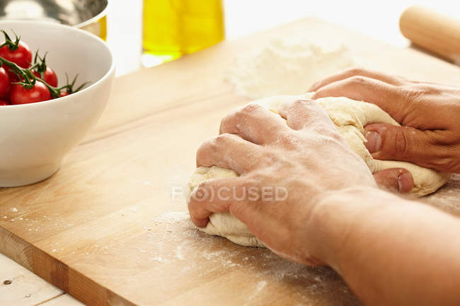 Hands kneading dough on wooden board — Stock Photo