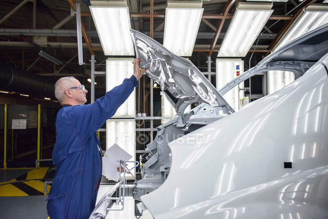 Travailleur inspectant la finition de la peinture du véhicule dans le poste d'inspection de l'usine automobile — Photo de stock