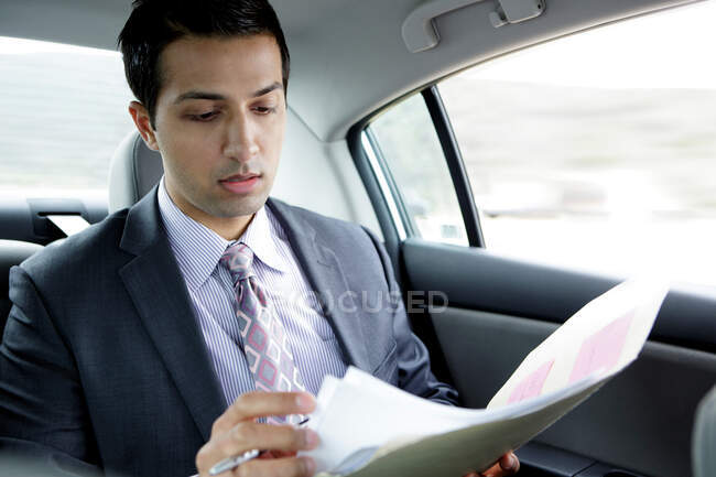 Businessman in back seat of car reading document — Stock Photo