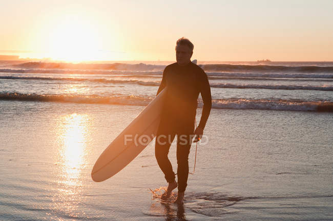 Surfeur marchant dans l'eau au coucher du soleil — Photo de stock