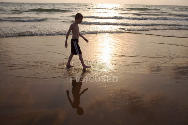 Garçon marche dans les vagues sur la plage — Photo de stock