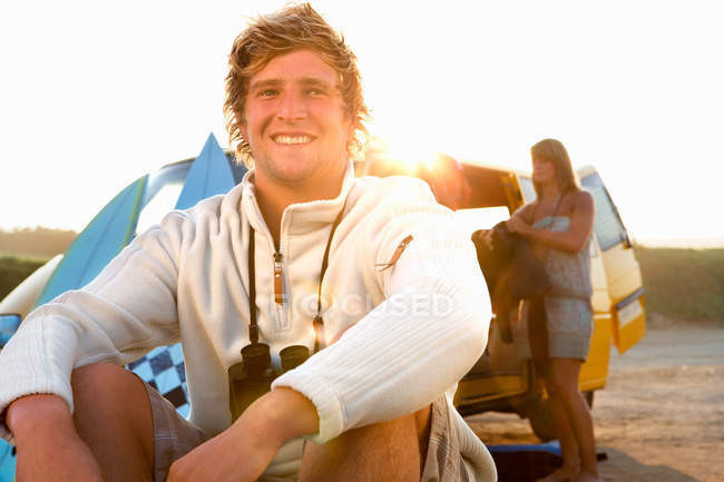 Hombre sentado en la playa sonriendo con la mujer - foto de stock