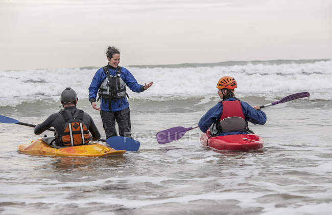 Instrutora feminina conversando com pessoas em caiaques no mar — Fotografia de Stock