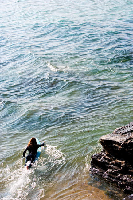 Вид сзади женщины, лежащей на доске для серфинга в воде — стоковое фото