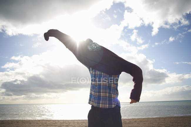 Homme mûr luttant pour mettre un pull à la plage — Photo de stock