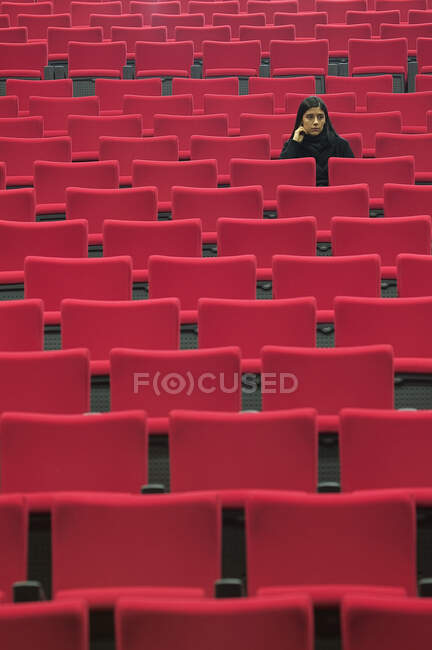 Mulher sentada sozinha no corredor de assentos vermelhos vazios — Fotografia de Stock