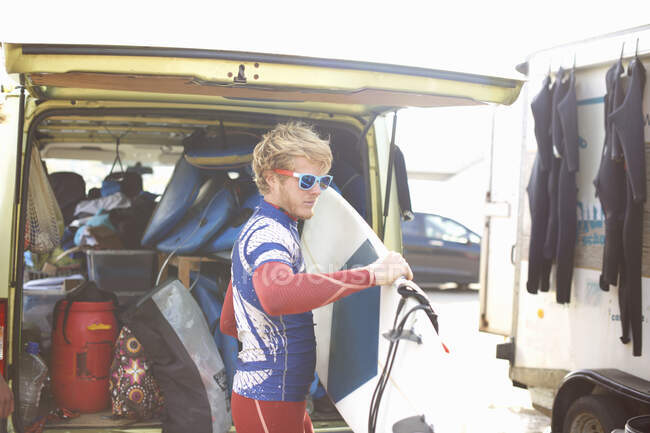 Чоловічий серфер стоїть біля відкритого фургона, тримає дошку для серфінгу — стокове фото