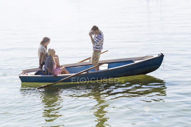 Side view of young man in boat on lake photographing women — Stock Photo
