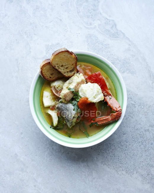 Still life with bowl of bouillabaisse soup and bread — Stock Photo