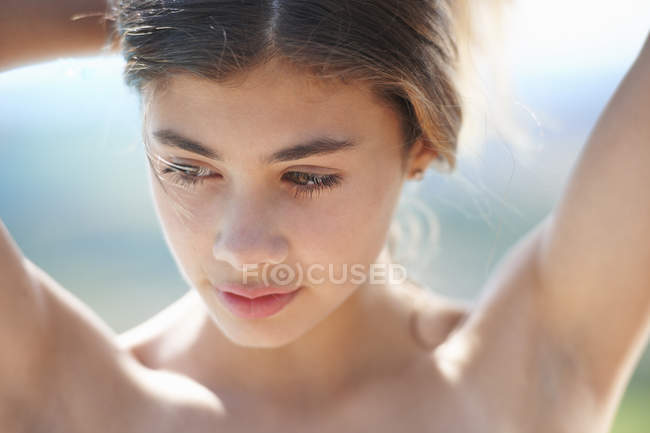 Портрет девочки-подростка, смотрящей вниз с поднятыми руками — стоковое фото