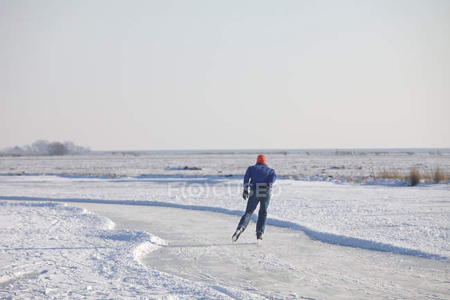 Rückansicht eines Mannes, der auf gefrorenem Fluss Schlittschuh läuft — Stockfoto