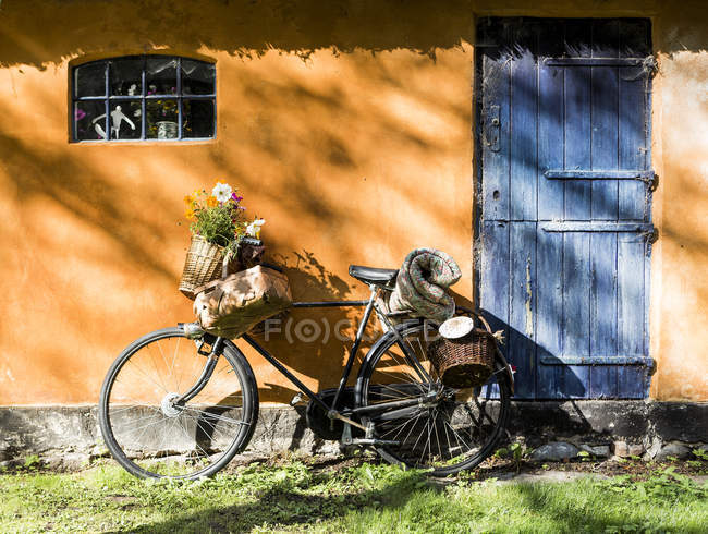 Bicicletta appoggiata alla parete del cottage con cestini da foraggio e fiori selvatici — Foto stock