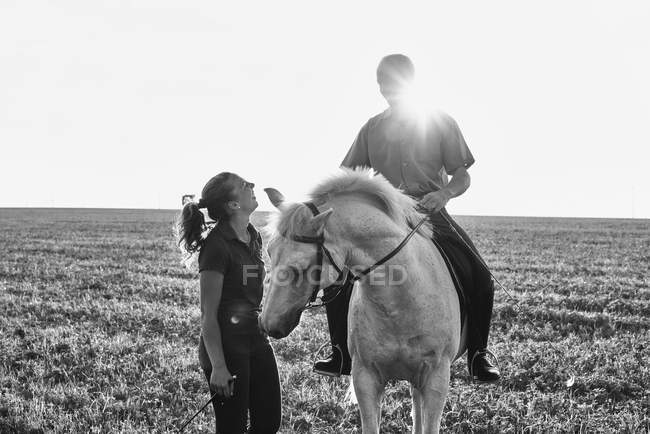 B & W imagem da mulher conversando com o homem montando cavalo cinza no campo — Fotografia de Stock