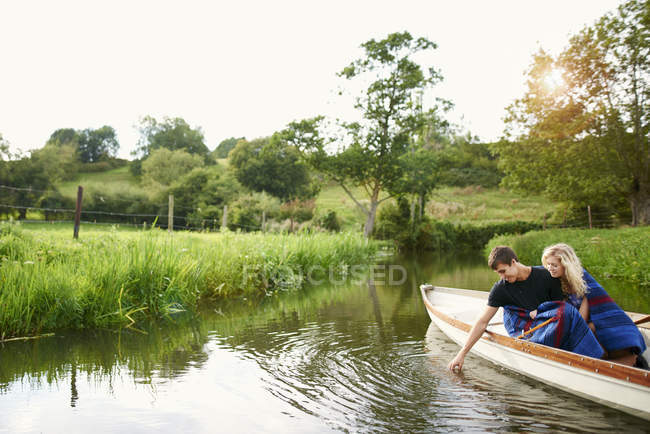 Young man with girlfriend touching water from river  rowing boat — Stock Photo