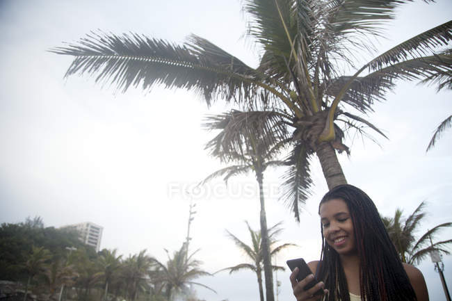 Jeune femme lisant des textes sur smartphone sur la plage d'Ipanema, Rio De Janeiro, Brésil — Photo de stock