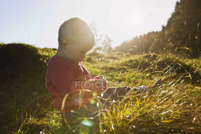 Baby girl sitting in field touching blades of grass — Stock Photo