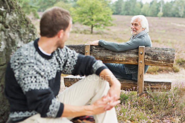 Senior man sitting on bench talking to mid adult man — Stock Photo