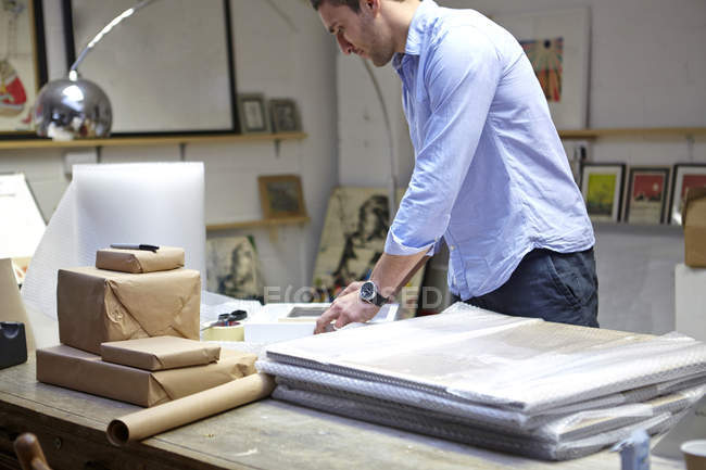 Homme enveloppant des cadres dans l'enveloppe de bulle sur la table dans l'atelier de encadreurs de photo — Photo de stock