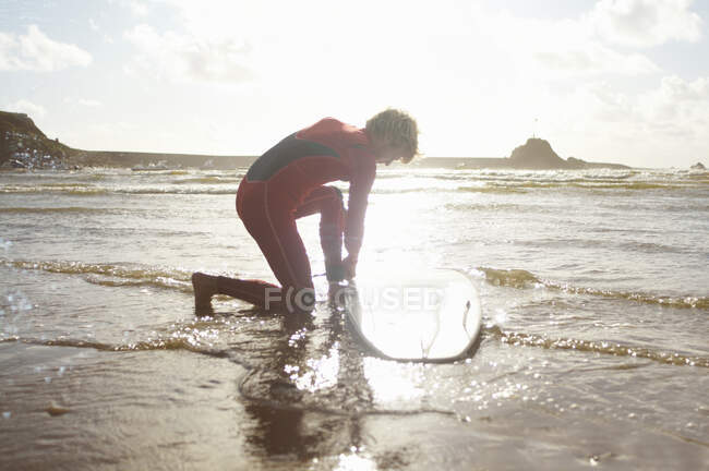 Surfeur masculin déliant la planche de surf de la cheville — Photo de stock