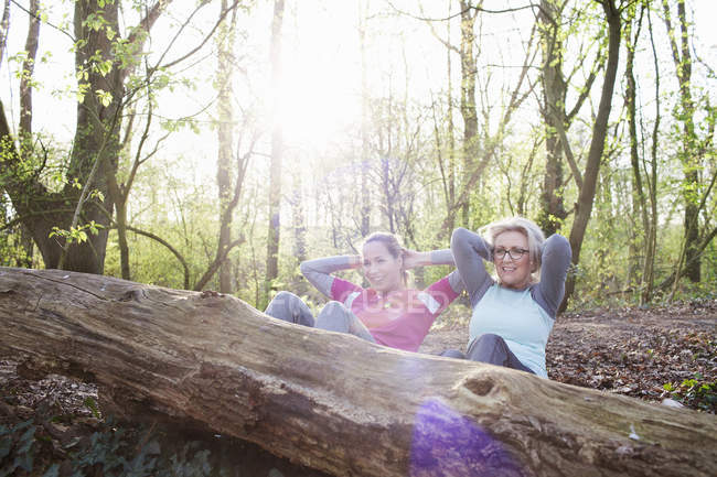 Mujeres en manos del bosque detrás de la cabeza haciendo sentarse contra el árbol caído - foto de stock