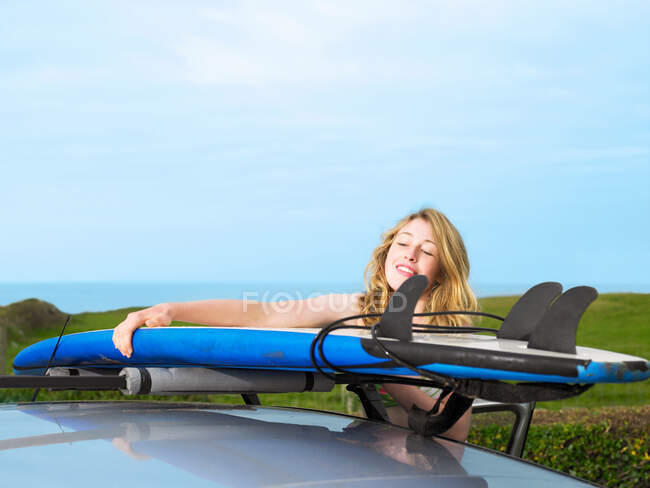 Femme prenant planche de surf sur le toit de la voiture — Photo de stock