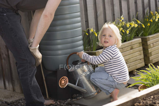 Boy filling watering can from water butt — Stock Photo