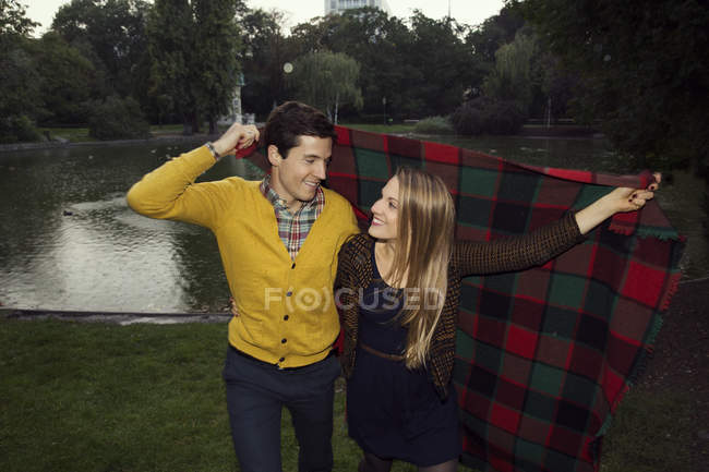 Young couple holding up blanket in park — Stock Photo