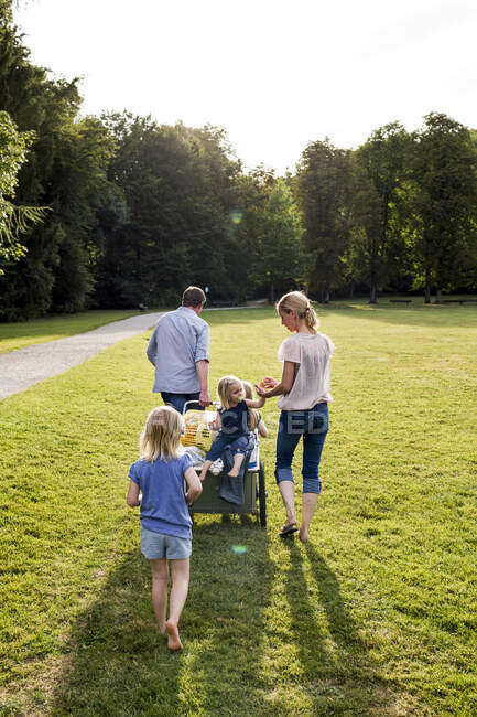 Vista trasera de los padres y tres niñas paseando por el parque - foto de stock
