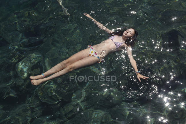 Chica flotando con los ojos cerrados en el mar - foto de stock