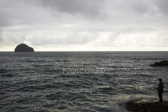 Silhouette Mann Seefischen aus Fels, Baumwipfel, Kornwand, uk — Stockfoto