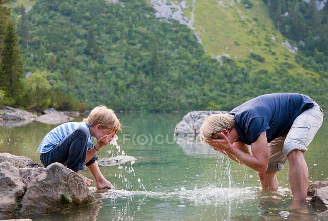 Chico lavándose la cara en un lago tranquilo - foto de stock