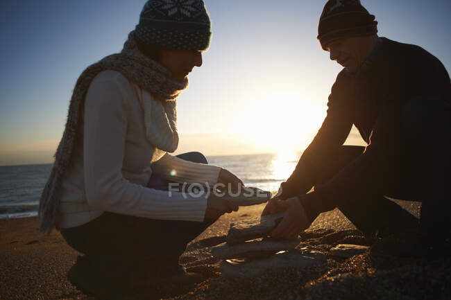 Mature couple stacking stones on beach at dusk — Stock Photo