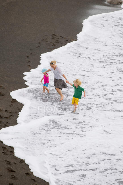 Mère et enfants marchant dans les vagues — Photo de stock
