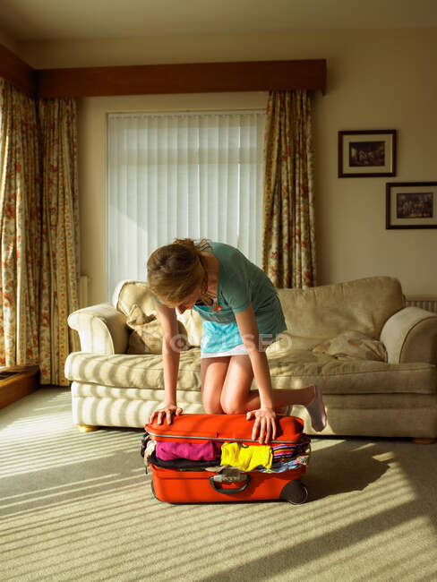 Молодая женщина пытается закрыть чемодан — стоковое фото