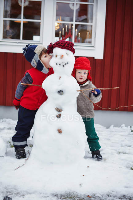 Niños de pie con muñeco de nieve - foto de stock