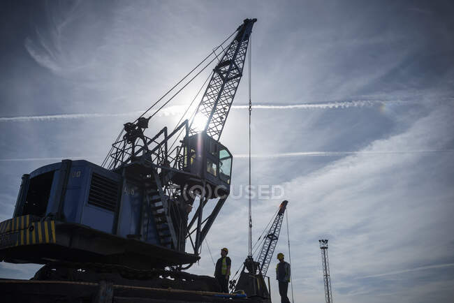 Visão de baixo ângulo de trabalhadores e guindaste em silhueta no porto — Fotografia de Stock