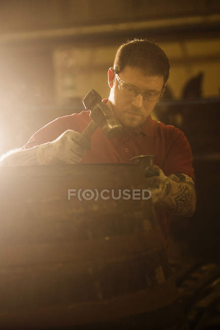 Male cooper using hammer in cooperage with whisky cask — Stock Photo