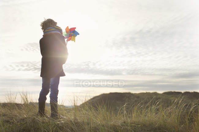 Rückansicht eines Jungen, der eine Papierwindmühle an der Küste hochhält — Stockfoto