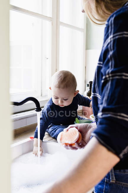 Baby boy touching running water at kitchen sink — Stock Photo