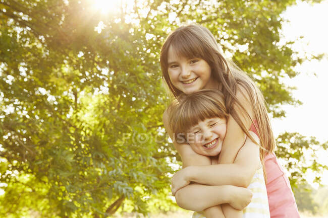Portrait of girl being hugged by big sister in park — Stock Photo