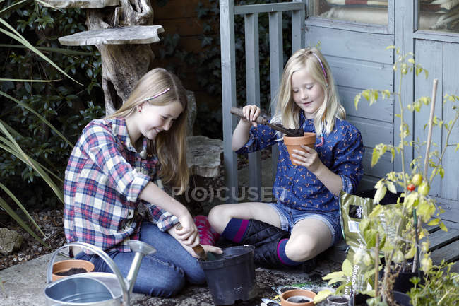 Дві дівчини в саду висаджують насіння в горщики — стокове фото